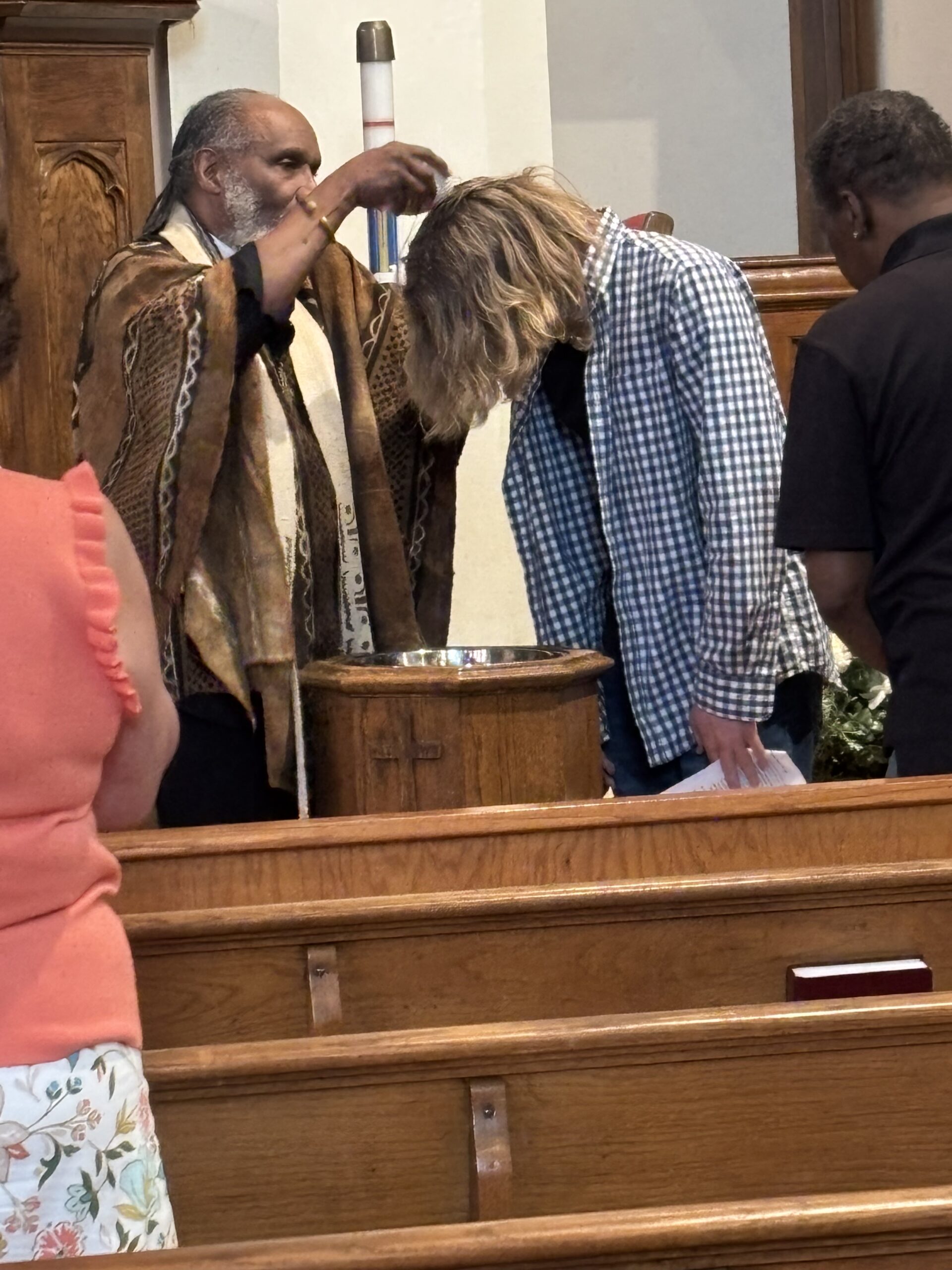 Pastor Starr baptizes young male congregant wearing checkered collared shirt.